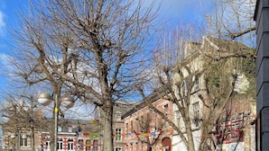 Une rue pavée avec des tables et des chaises installées à l’extérieur, des arbres et des bâtiments en arrière-plan.