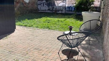 Een terras met een metselstenen vloer, twee metalen stoelen en een grote terracotta pot.