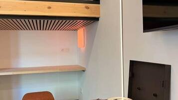 A bunk bed with a wooden headboard, a small stool, and a vintage radio on a wooden table.