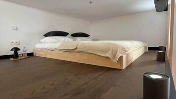 Un dormitorio con cama de madera, una mesita de noche pequeña, una lámpara y un enchufe en la pared.