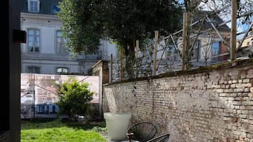 Une terrasse en briques avec deux chaises en métal et un grand bac à fleurs.