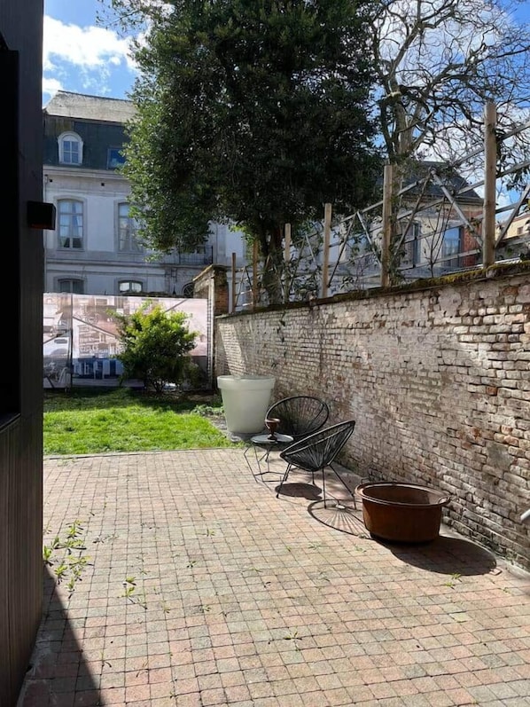 Un patio in mattoni con due sedie in metallo e un vaso grande.
