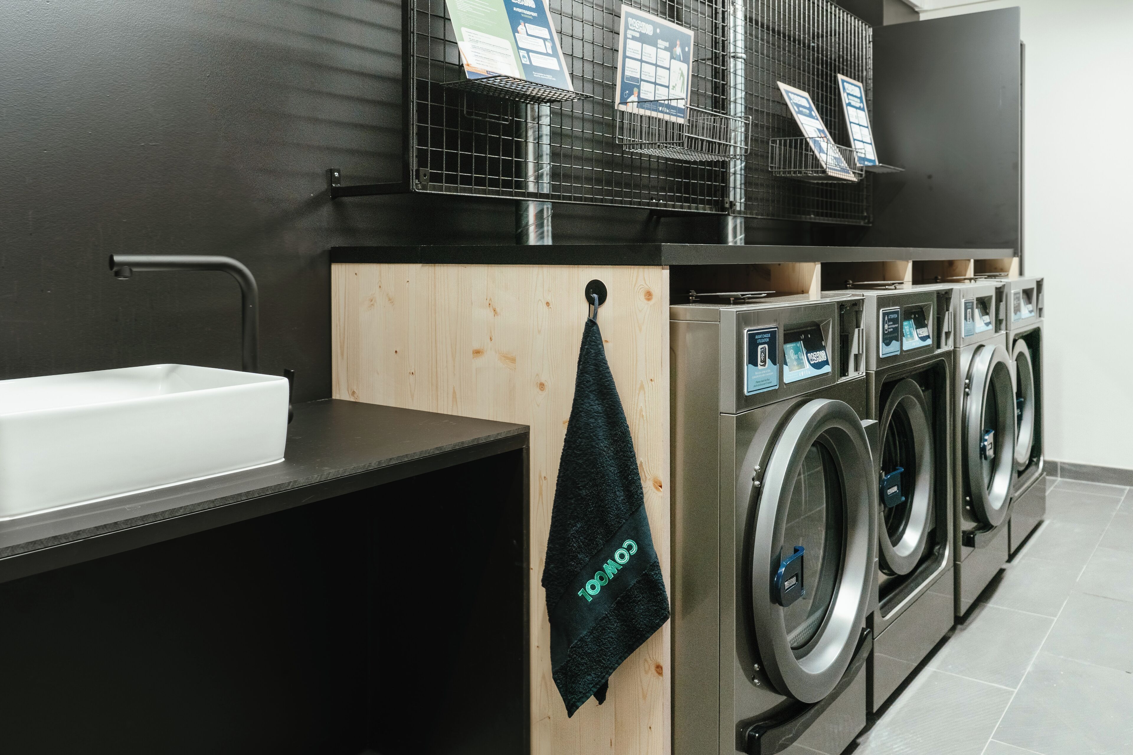 A modern laundry facility with a sink, multiple washing machines, and a towel hanging on a rack.