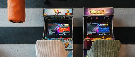 Two retro video game arcade machines with colorful graphics, a punching bag, and two chairs in front of a striped wall.