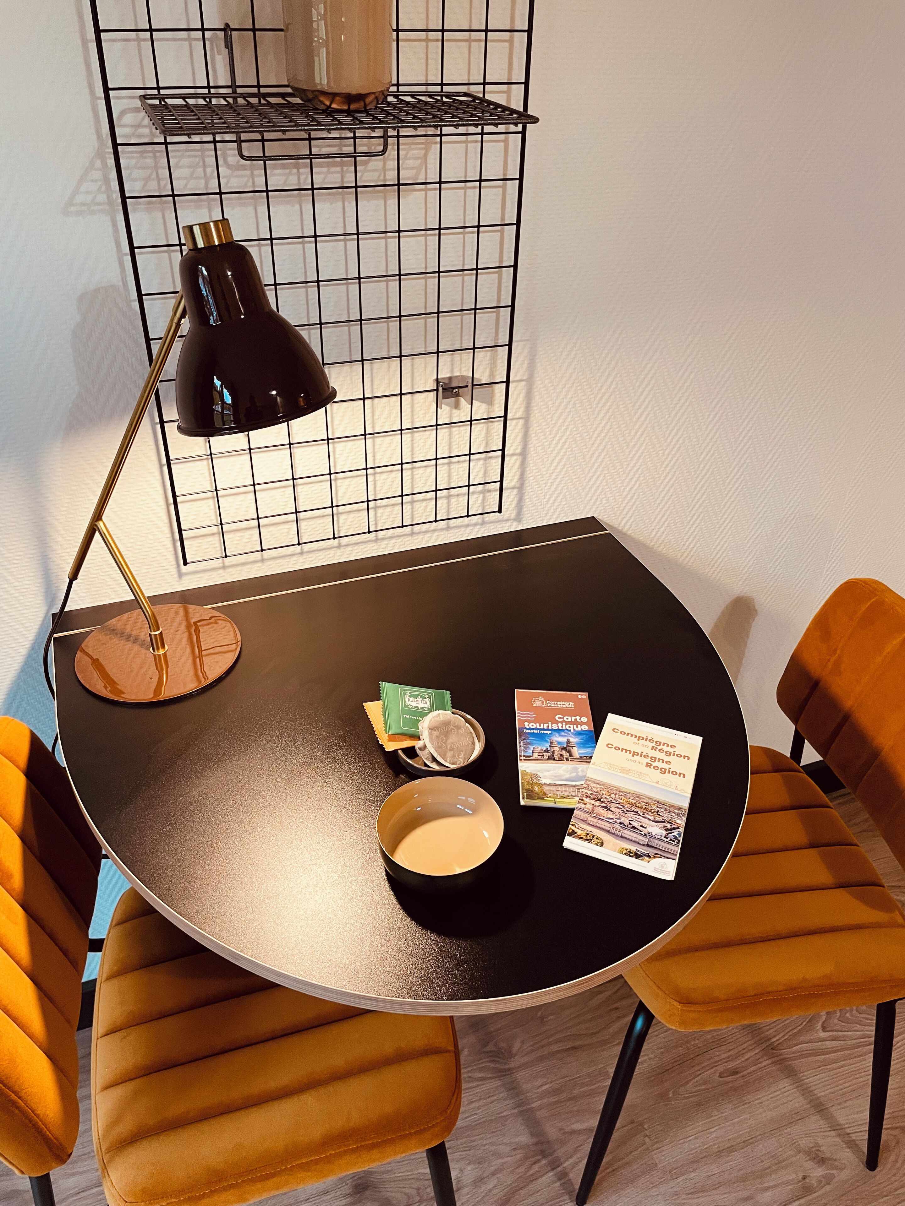 A small round table with a black lamp, a bowl, and some brochures. There are two orange chairs around the table.