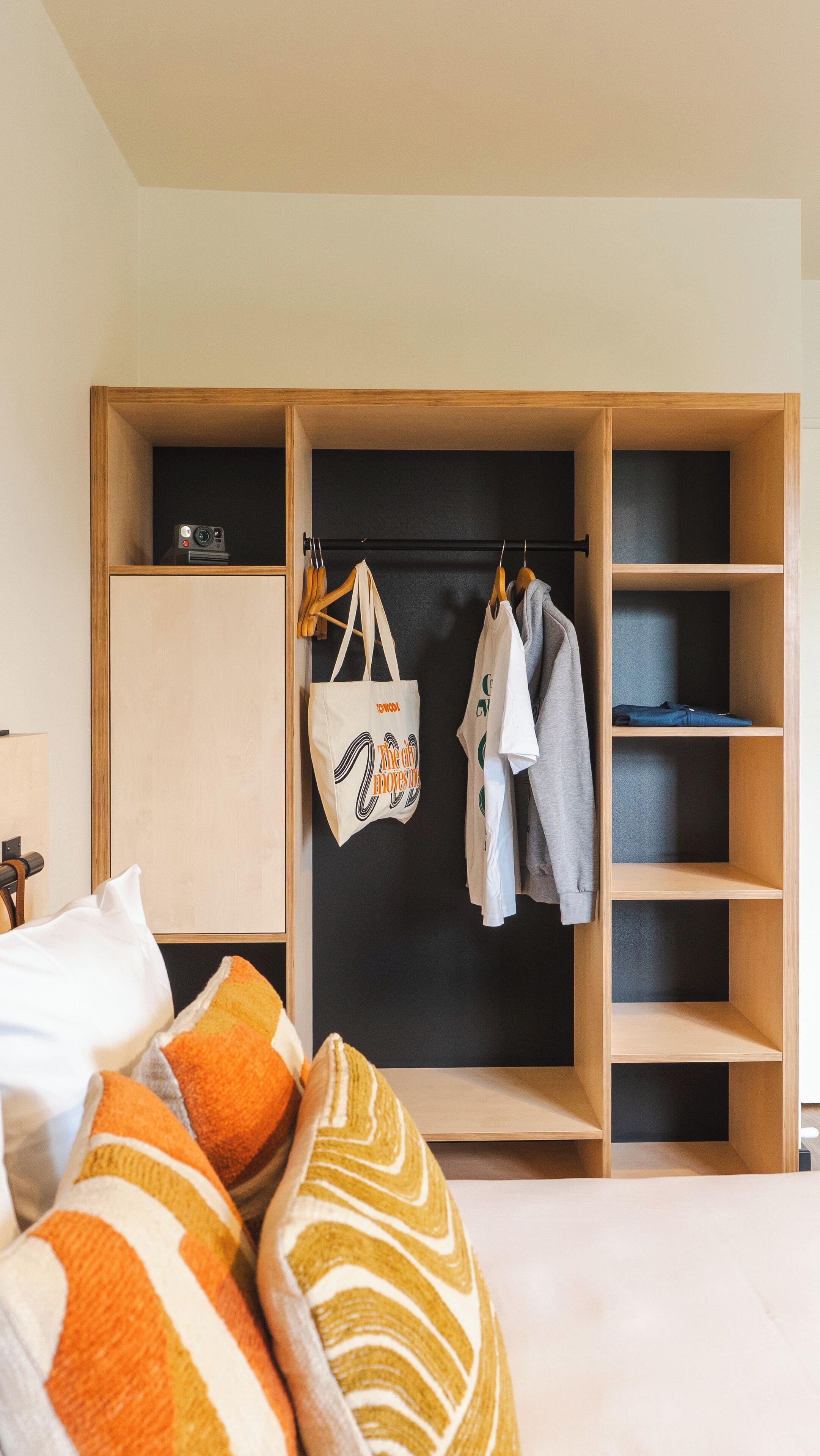A bedroom with a bed, a wardrobe with multiple shelves, and a hanging rod for clothes.