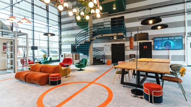 A spacious indoor area with a large wooden table, colorful seating, and a visible staircase. - Cowool Compiègne (Compiègne)