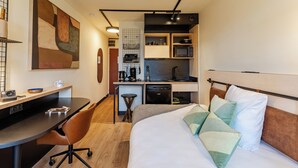 A compact hotel room with a bed, a desk, a chair, a kitchenette, and a small dining area. - Cowool Compiègne (Compiègne)