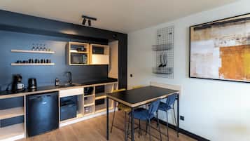 A compact kitchen with a refrigerator, coffee maker, and shelves with kitchenware.