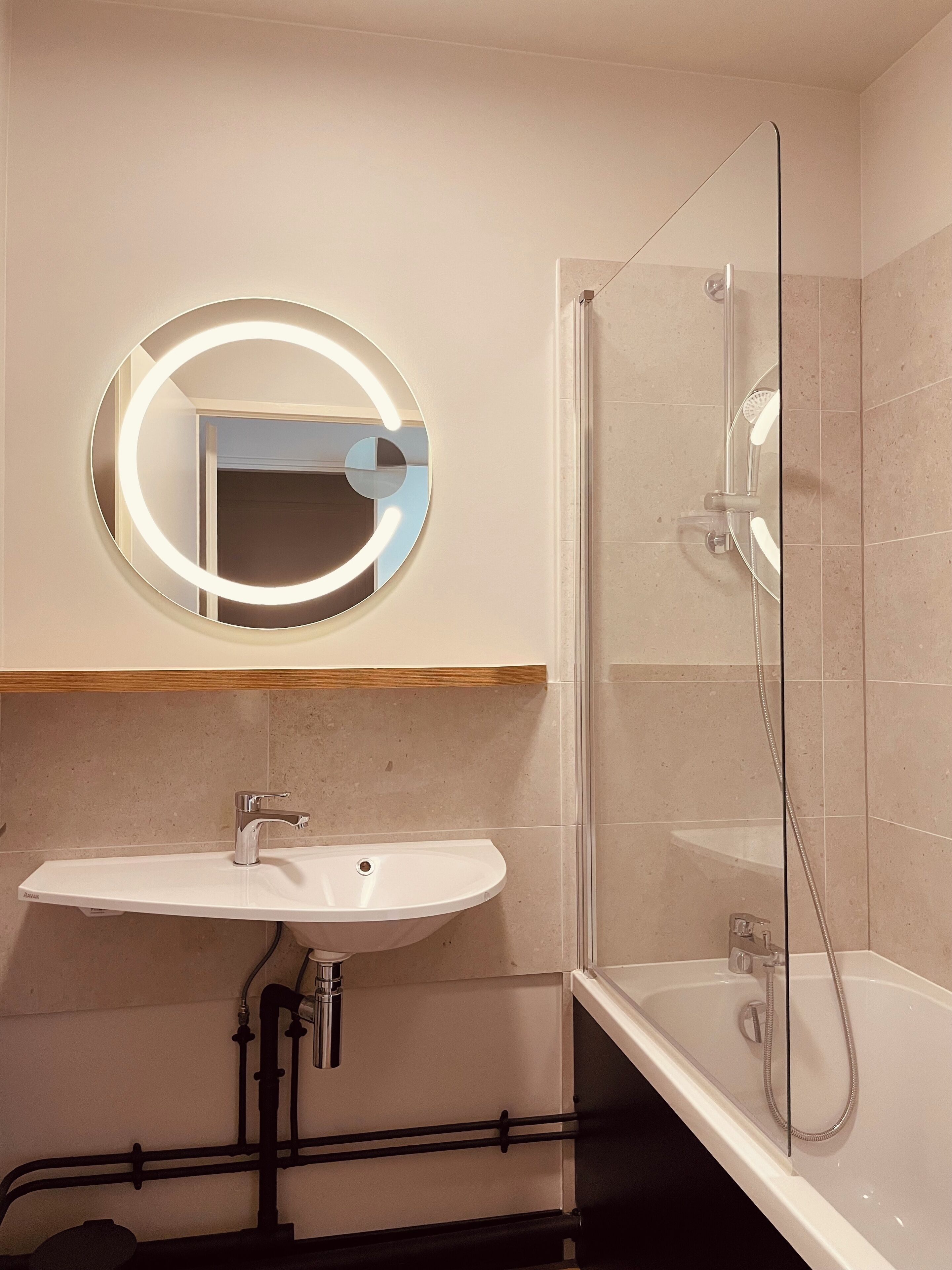 A bathroom with a round mirror, a sink, and a glass-enclosed shower.