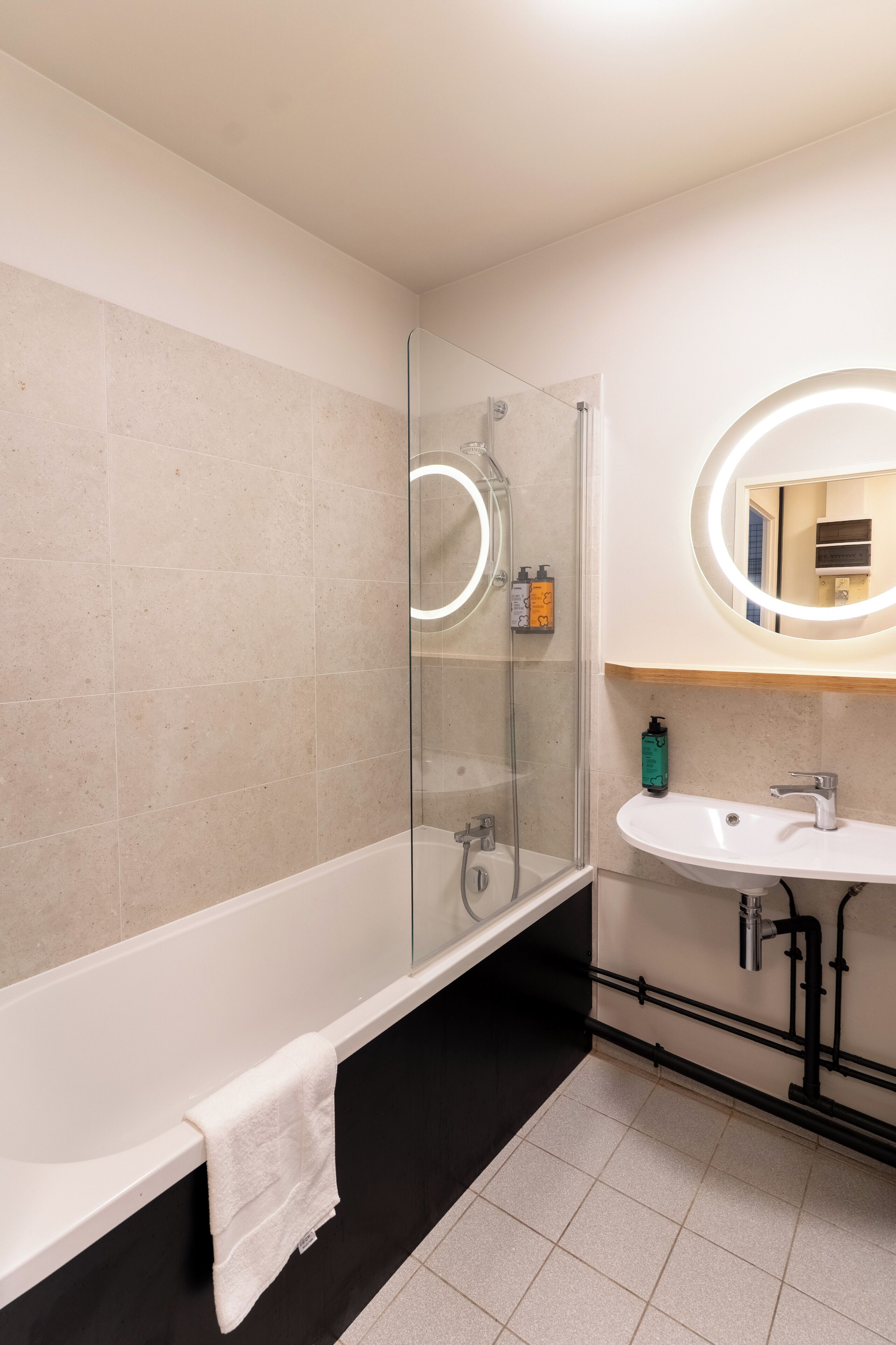 A modern bathroom with a glass-enclosed shower, a white bathtub, and a sink with a mirror above it.