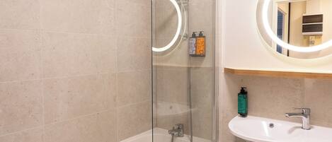 A modern bathroom with a glass-enclosed shower, a white bathtub, and a sink with a mirror above it.