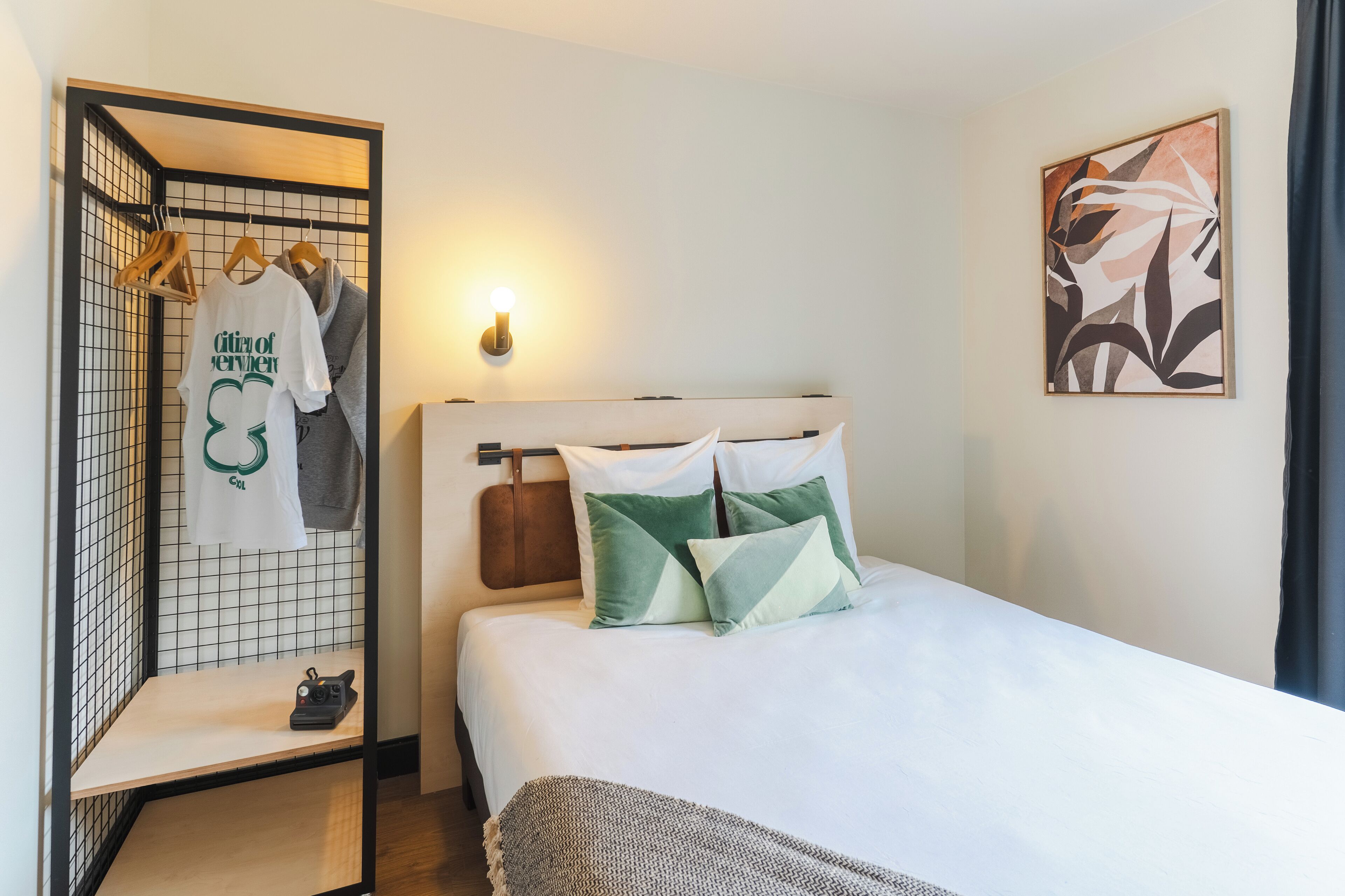 A neatly made bed with pillows, a hanging clothing rack, and a wall-mounted light.