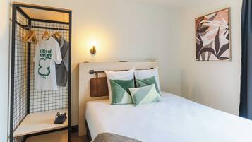 A neatly made bed with pillows, a hanging clothing rack, and a wall-mounted light.