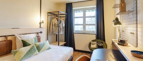 Habitación de hotel con cama, escritorio, silla, ventana y armario.