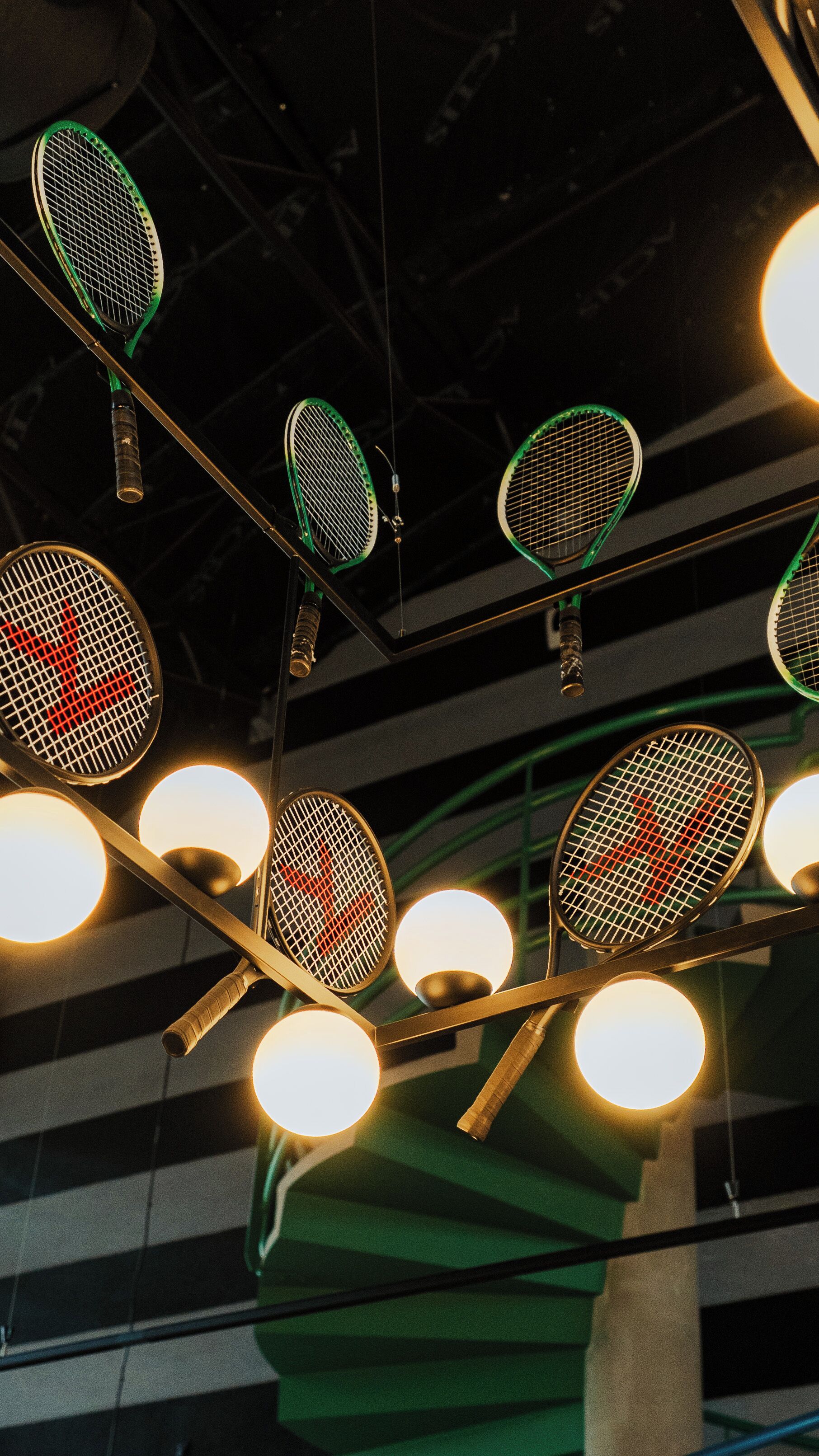 Un techo con varias raquetas de tenis colgando, cada una unida a una lámpara circular.
