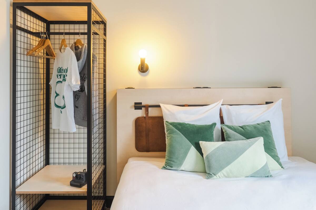 A neatly organized room with a bed, a hanging clothing rack, and a wall-mounted light fixture.