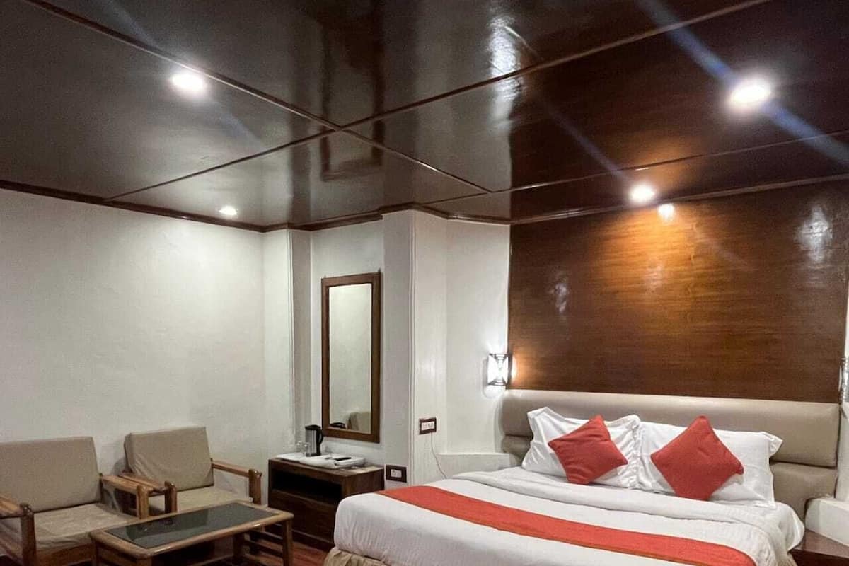 A hotel room with a large bed, a wooden chair, a small table, and a nightstand.