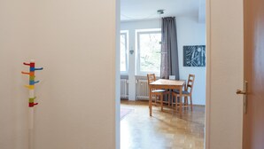 A room with a wooden parquet floor, a white wall with a colorful coat rack, and a view into a dining area with a table and chairs. - Guesthouse Elena Apartment 23 (Kassel)