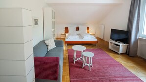 A modern hotel room with a bed, a sofa, two small tables, a TV, and a red rug. - Guesthouse Elena Apartment 23 (Kassel)