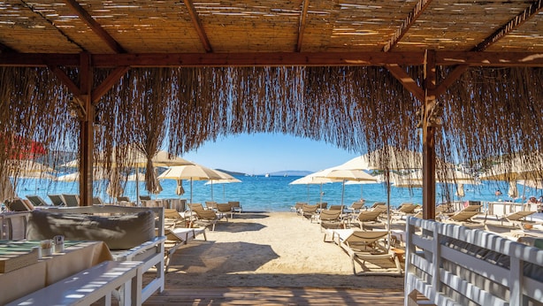 Un salon de plage doté d’une terrasse en bois, de chaises longues et de parasols, offrant une vue sur la mer.