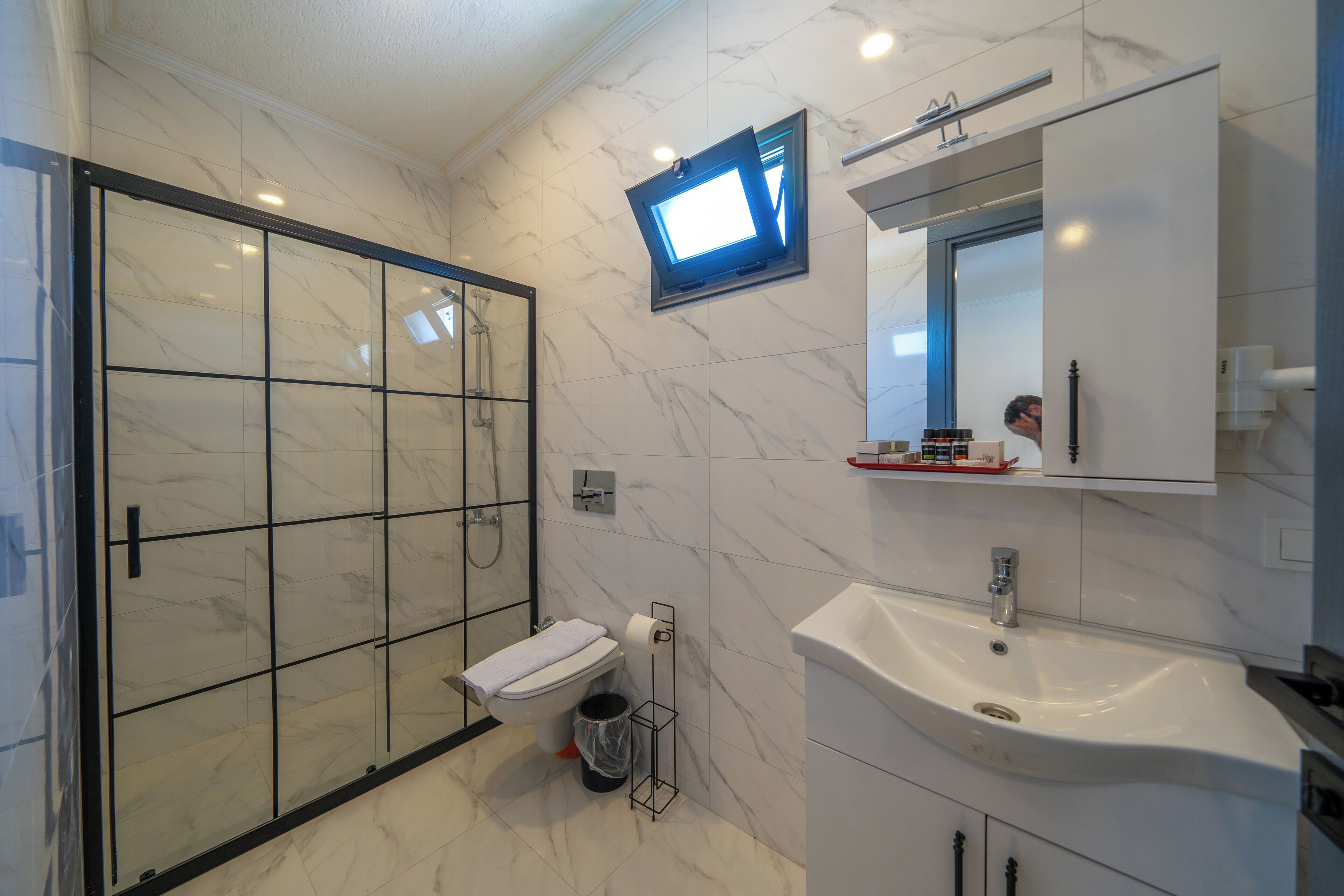 A modern bathroom with a glass shower enclosure, a white sink, and a mounted television.