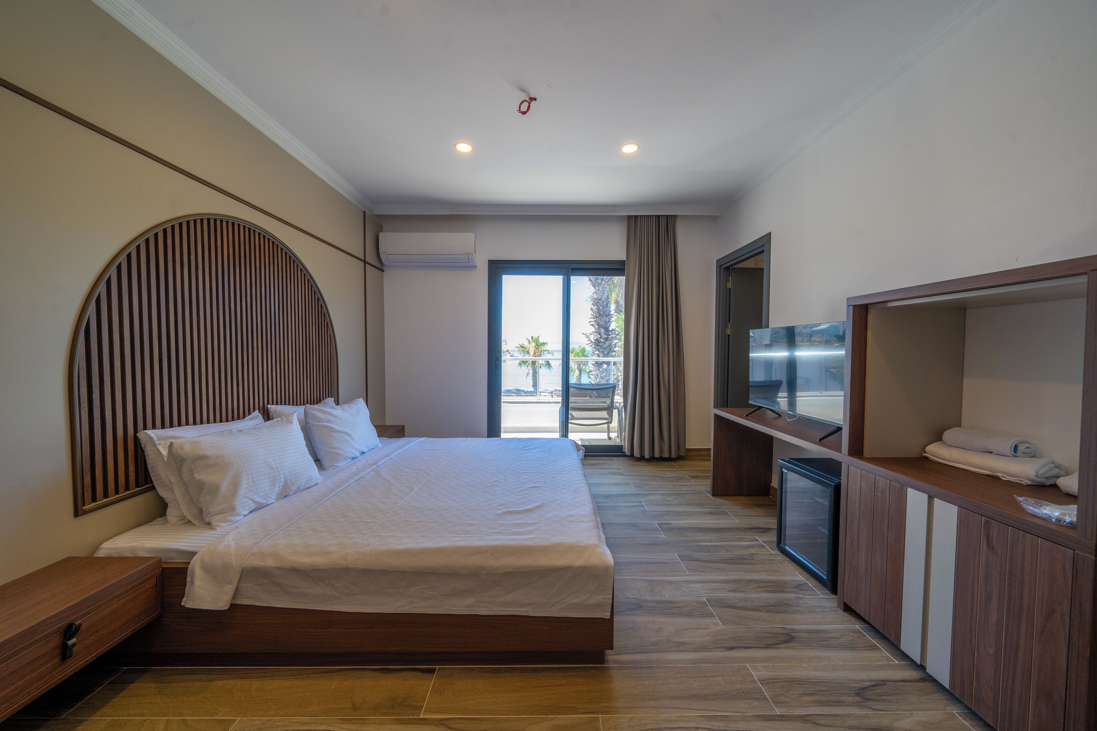 A modern hotel room with a large bed, a TV, and a balcony with a view.