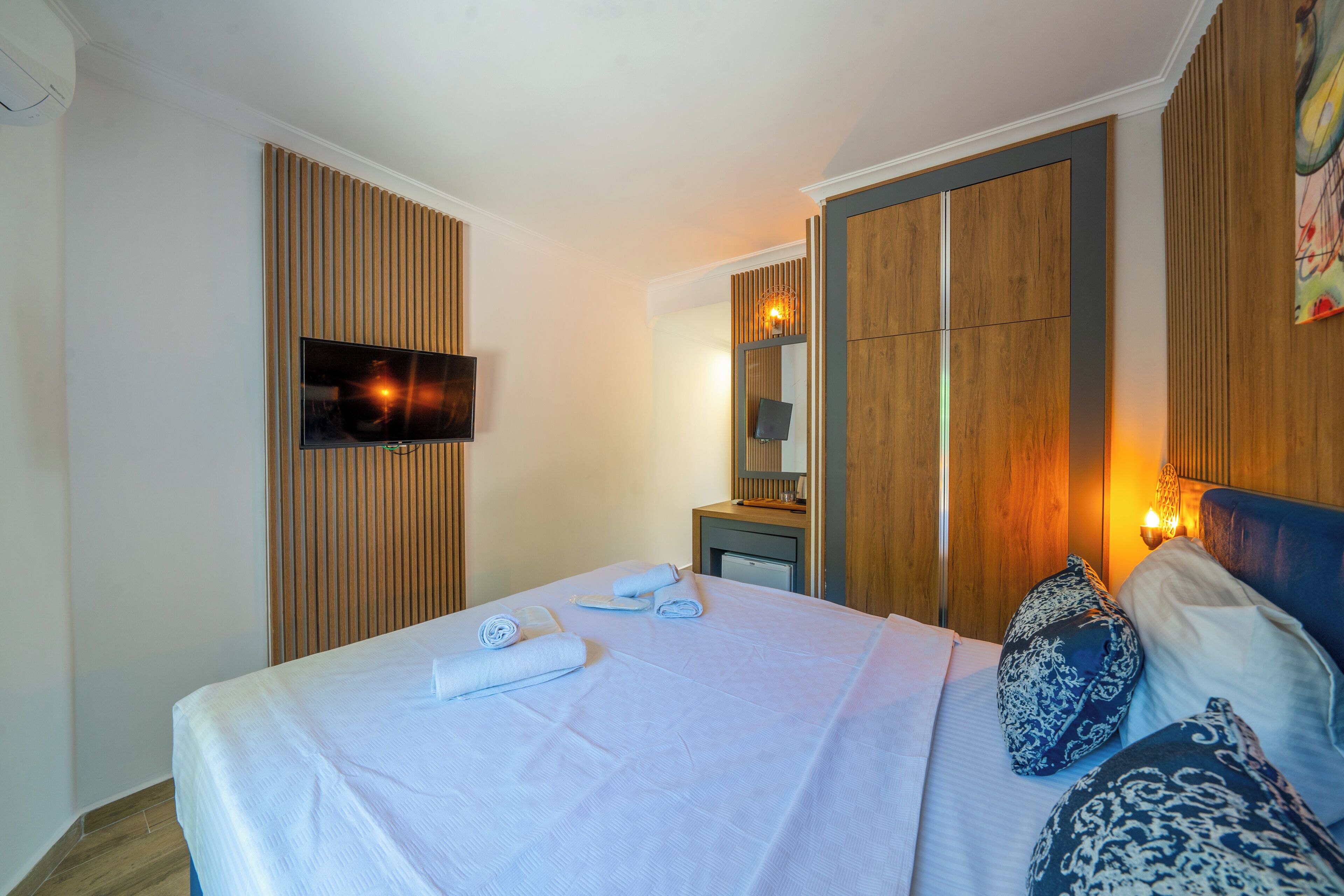 A hotel room with a bed, a television, a wooden wardrobe, and a mirror.