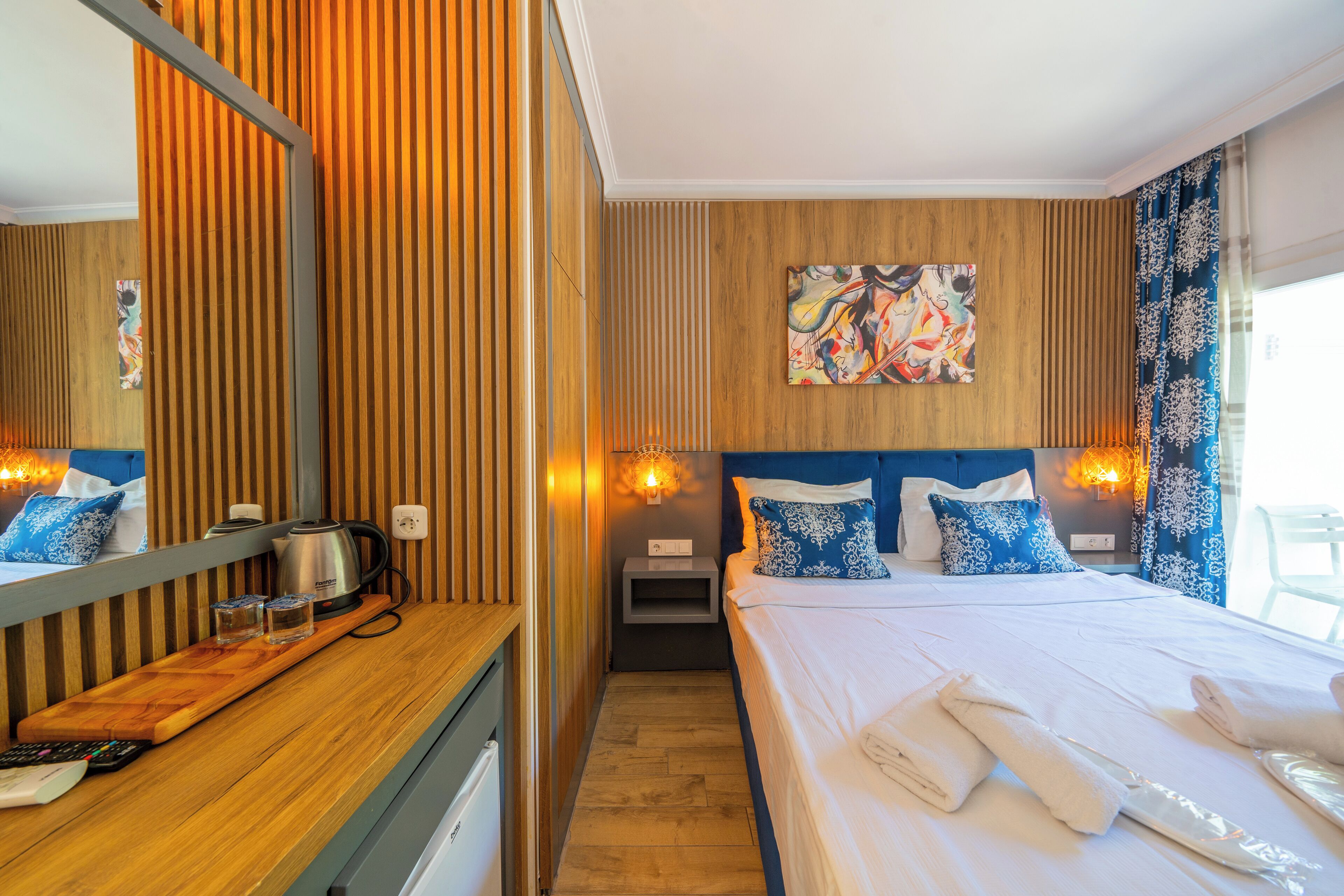 Une chambre d’hôtel avec un mur lambrissé en bois, un grand lit avec une literie bleue et blanche, un tableau accroché au mur et une table de chevet avec une lampe.