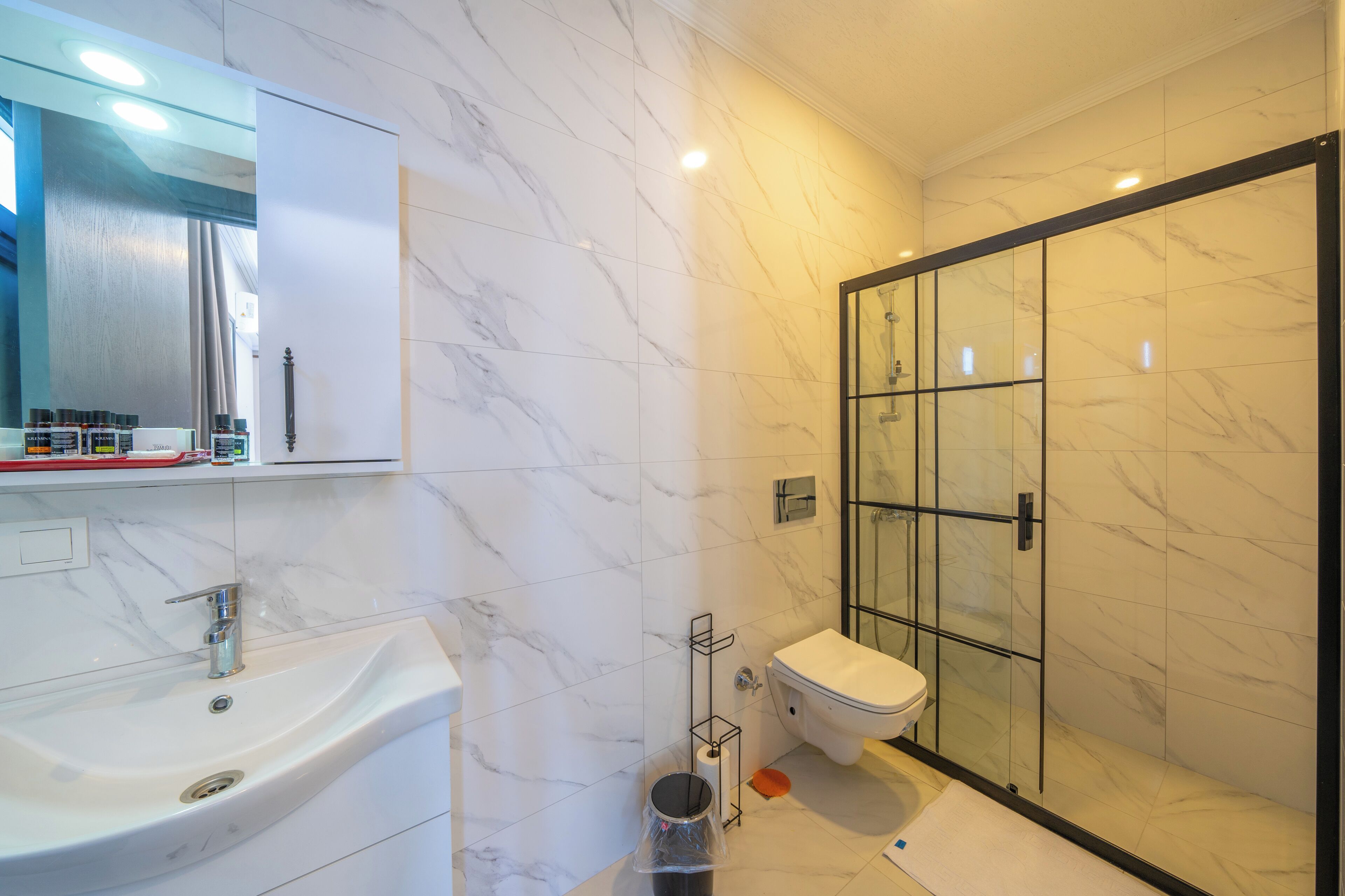 A modern bathroom with a marble sink, toilet, and glass shower enclosure.
