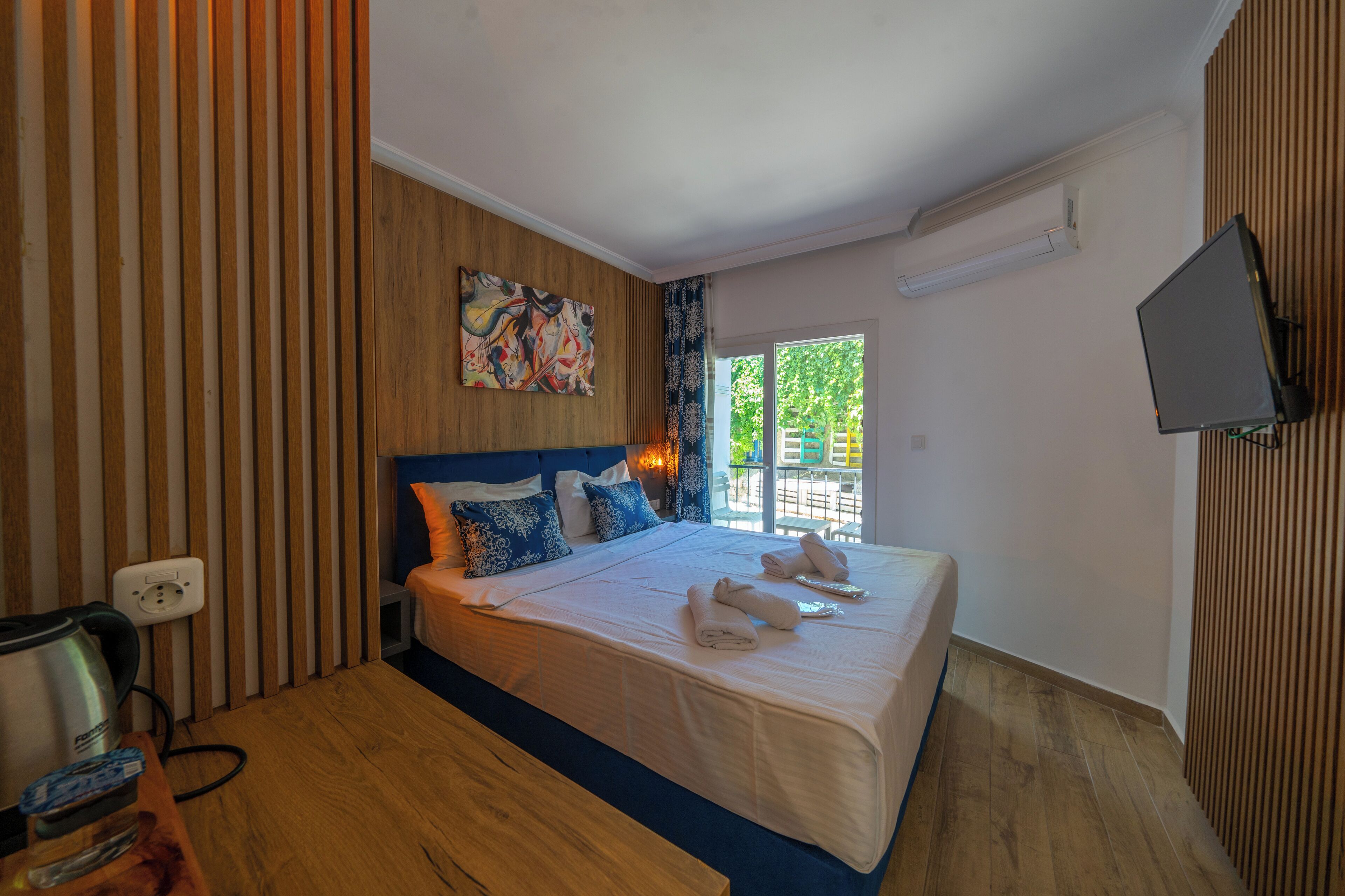 Une chambre d’hôtel avec un lit, une télévision, un tableau et une fenêtre donnant sur un paysage verdoyant.
