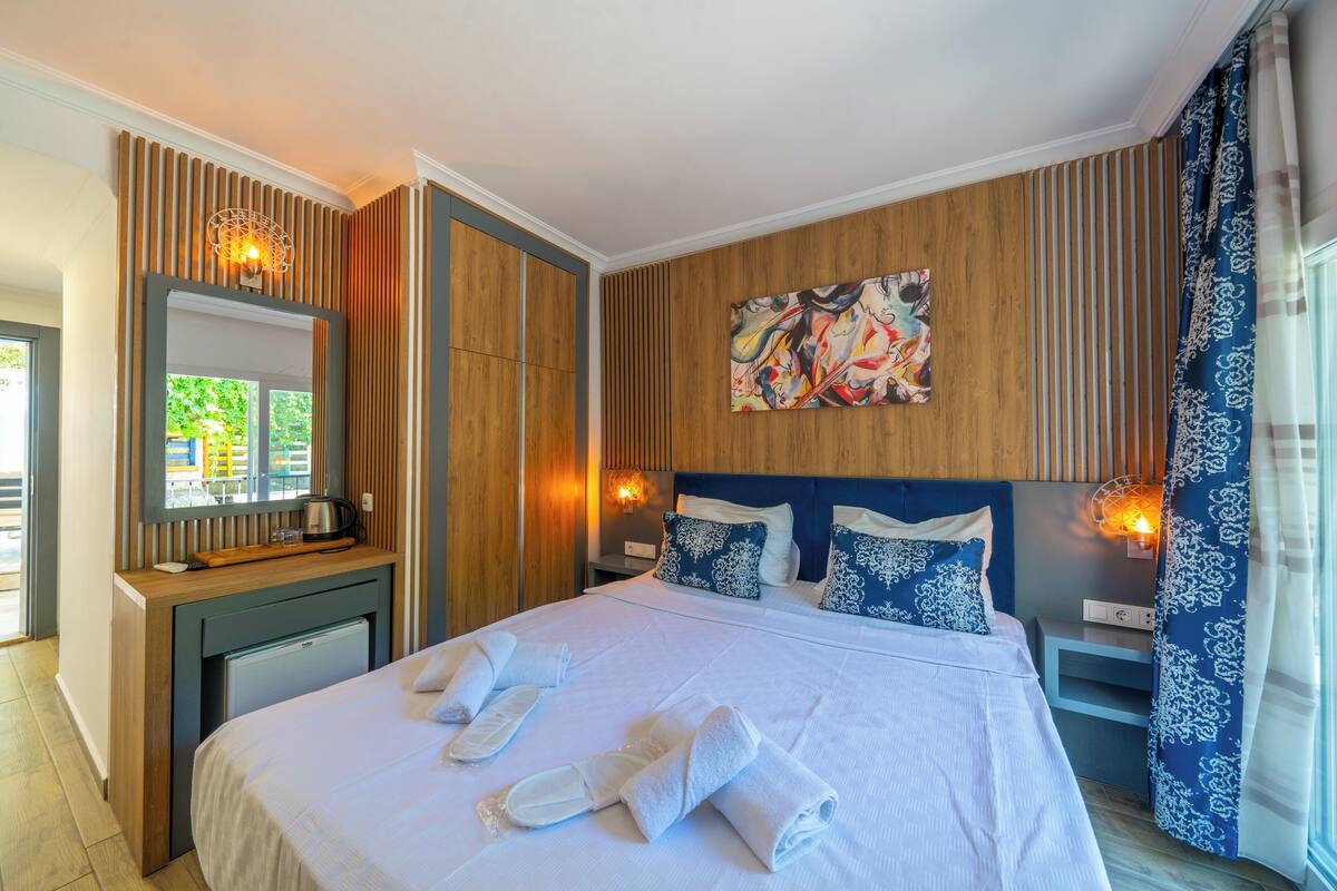 Un lit bien fait, avec des serviettes, une tête de lit en bois, un tableau et une fenêtre avec des rideaux.