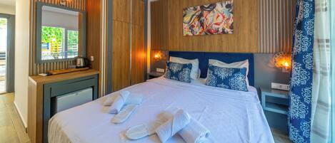 A neatly made bed with towels, a wooden headboard, a painting, and a window with curtains.