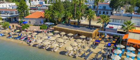 A beachside hotel with sun loungers, umbrellas, and a thatched-roof building.