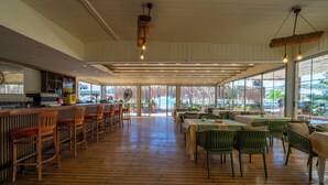 Un grand espace intérieur doté d’un plancher en bois, de chaises vertes, de tables et d’un coin bar avec des tabourets.