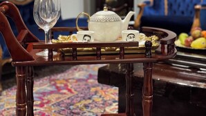 A room with a wooden table set for tea, a blue sofa, a large clock, and a colorful rug. - Flexistay Hotel (Cape Town)