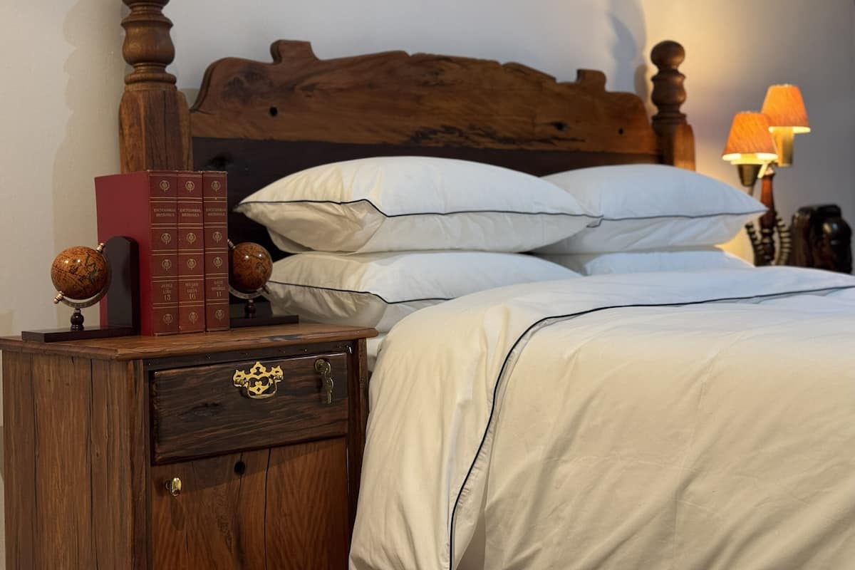 A neatly made bed with white linens, a wooden headboard, a nightstand with a globe and books, and a lamp on the side.