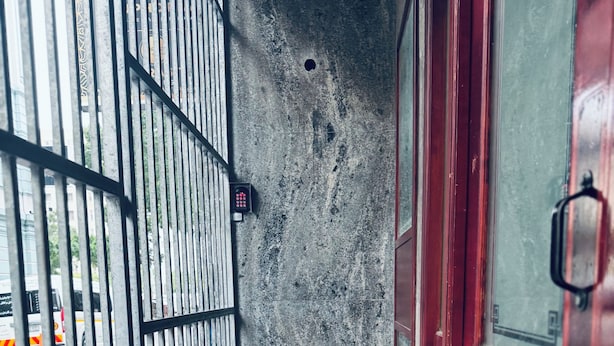 A narrow corridor with a metal gate, a red door, and a concrete wall. - Flexistay Hotel (Cape Town)