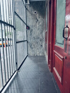 Een smalle gang met een metalen poort, een rode deur en een betonnen muur.
