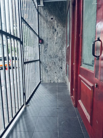 A narrow corridor with a metal gate, a red door, and a concrete wall.