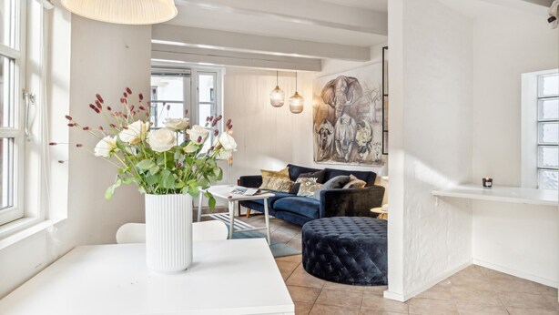 Un salon moderne avec un canapé blanc, un pouf bleu et une table basse blanche. Un vase avec des fleurs blanches est posé sur la table basse.