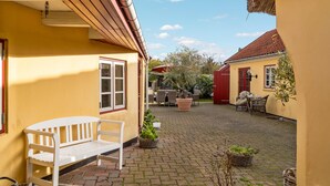 Une cour avec un banc blanc, des chaises en osier et des plantes en pot.