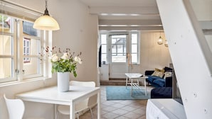 Un espace de vie moderne avec une table à manger blanche, des chaises, un canapé blanc et un canapé bleu. On peut voir un vase blanc rempli de fleurs sur la table à manger.