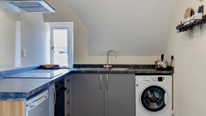 A compact kitchen with a built-in dishwasher, a washing machine, and a sink. - Cozy Corsham Apartment With 2 Bedrooms (Corsham)