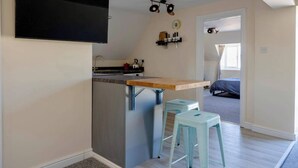 A compact kitchen with a wooden countertop, two light blue stools, and a black TV mounted on the wall. - Cozy Corsham Apartment With 2 Bedrooms (Corsham)