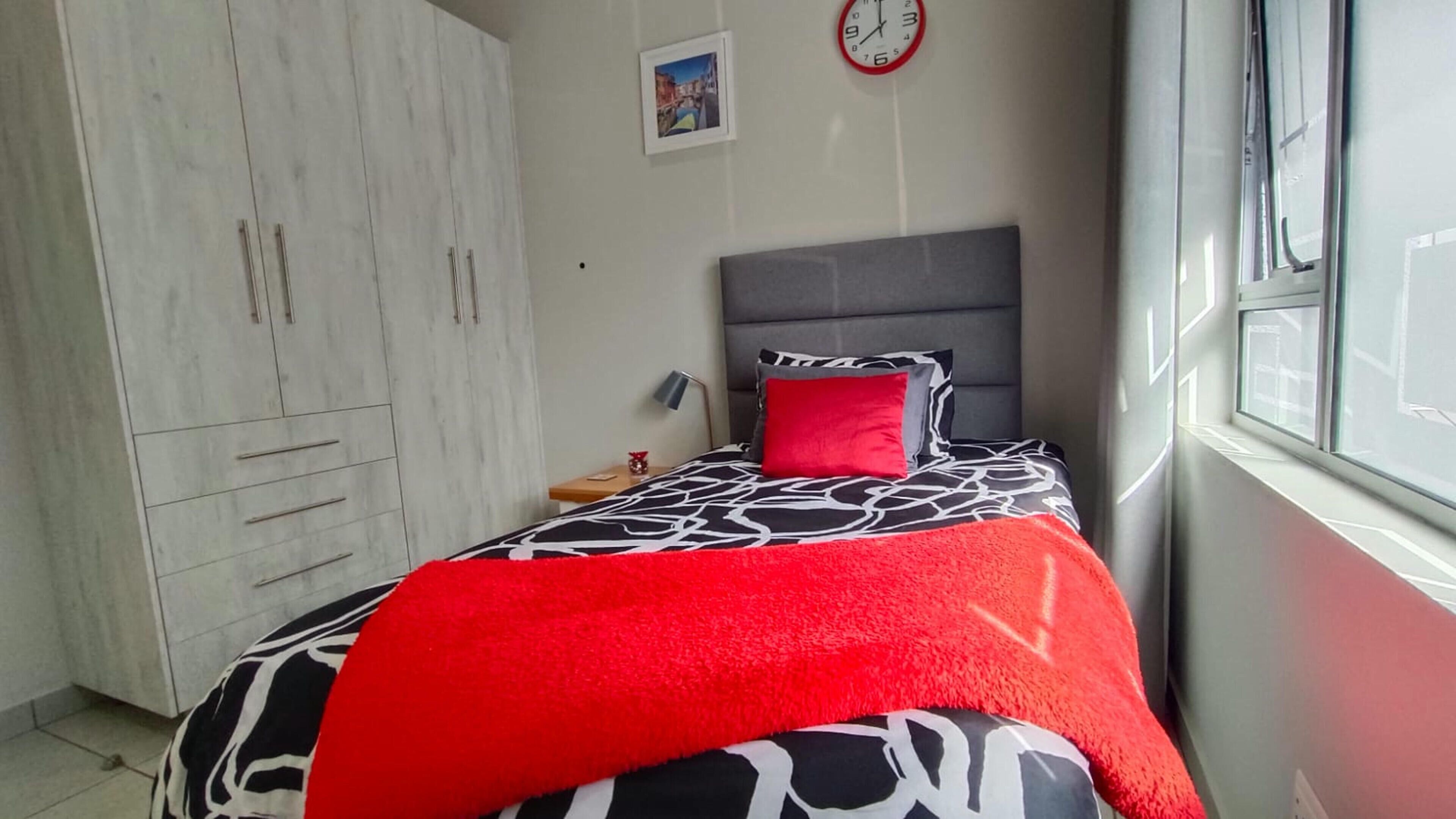 A bedroom with a bed, a wardrobe, a clock, and a window.