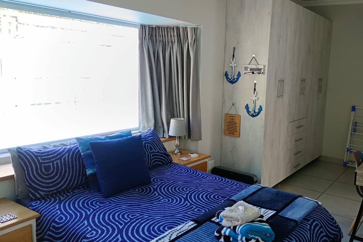 A bedroom with a bed, a desk, a chair, a window with curtains, and a wardrobe.