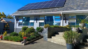A modern building with solar panels, a cross on the facade, and a well-maintained garden.
