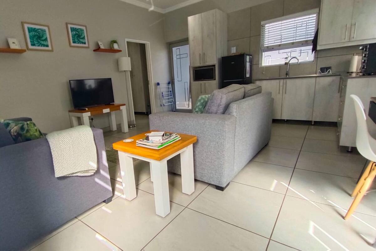 A living room with a sofa, a coffee table, a TV, and a kitchen area with cabinets and a refrigerator.