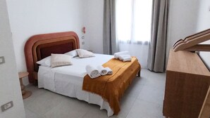 A hotel room with a bed, a wooden desk, and a window with curtains. - Domus Luxi - Teulada Design Apartment | Style and Comfort (Teulada)